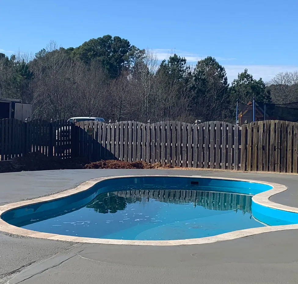 Concrete pool deck surrounding a backyard swimming pool in Meridianville, AL
